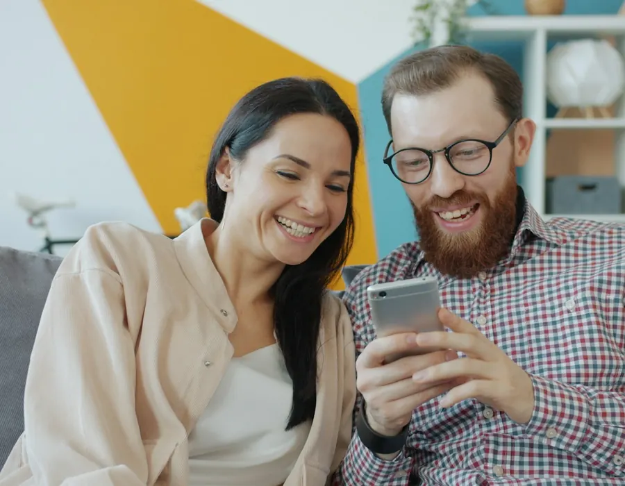 Couple laughing together while looking at a phone at home