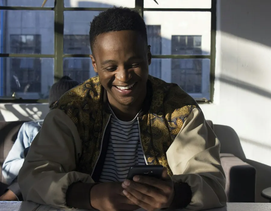 Smiling man looking at his phone in a sunny apartment
