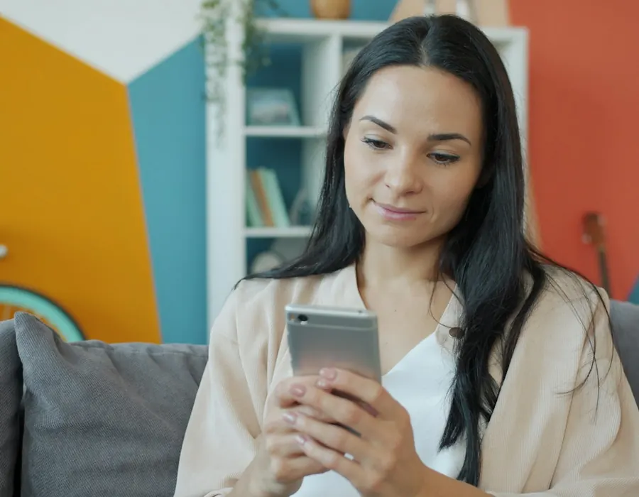 Woman smiling at her phone on the couch at home