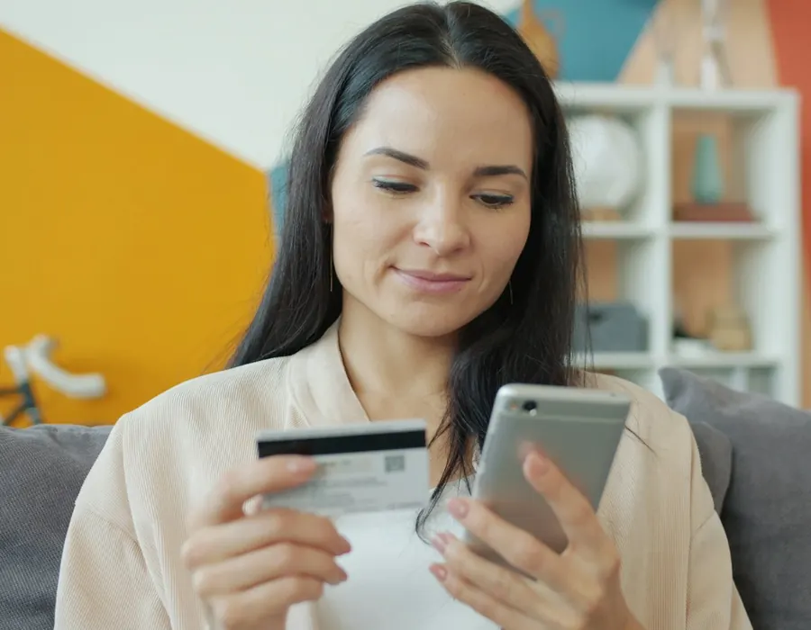Woman paying a bill on her phone with her debit card at home